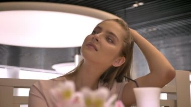 Genç güzel kız kameraya, kahve, dokunaklı saç içme izlerken rastaurant içinde oturuyor, kavram sakin ol