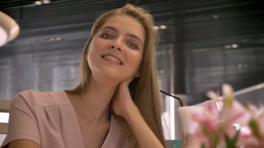 Genç güzel kız kameraya, gülümseyen, kahve içme izlerken rastaurant içinde oturuyor, kavram sakin ol