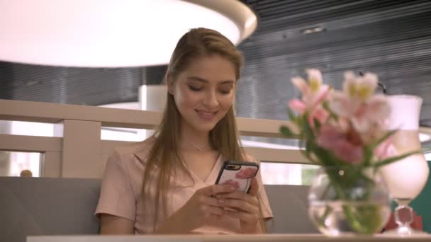 Krásná mladá dívka sedí v rastaurant, chatování na smartphone, pití kávy, relax koncept, komunikační koncept — Stock video