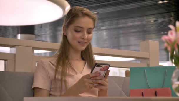 Menina bonita jovem está sentado em rastaurant, conversando no smartphone, beber café, sorrindo, assistindo a câmera, relaxe conceito, conceito de comunicação — Vídeo de Stock