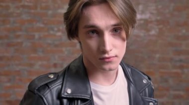 Kameraya dönüm ve dokunuyorsun onun saç, tuğla arka plan siyah deri ceketli genç çekici adamı