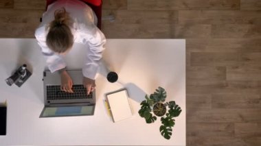 Genç kadın bilim adamı mikroskobu arıyorsunuz ve tipik dizüstü bilgisayar, topshot, Tıbbi laboratuar araştırmaları üzerinde beyaz önlük