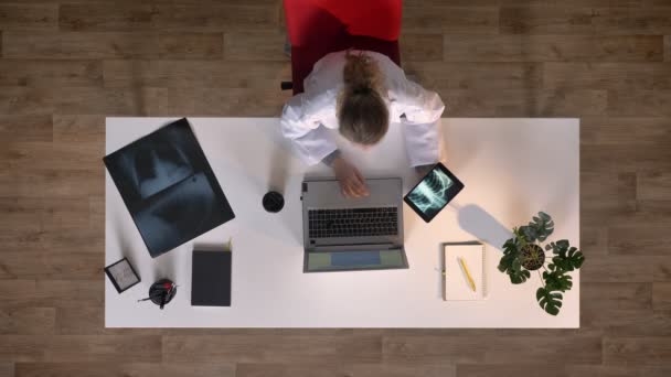 Unga kvinnliga läkare håller tablett med röntgenbilden och skriva på laptop, topshot, medicinska begrepp — Stockvideo