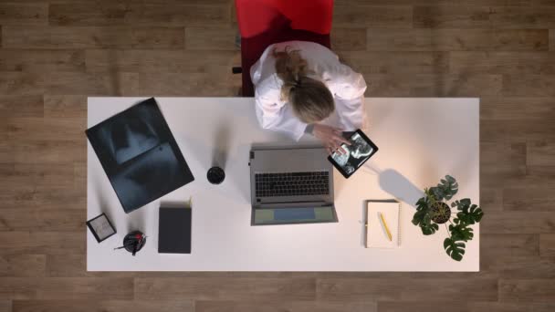 Doctora joven sosteniendo la tableta con imagen de rayos X y beber café, topshot, sentado en la mesa, concepto médico — Vídeos de Stock