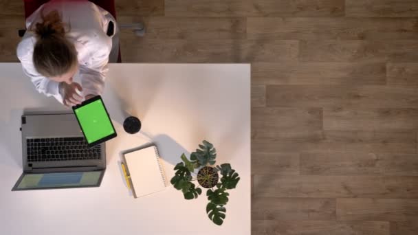 Doctora joven en bata blanca usando tableta con cromakey, topshot, sentada en la mesa con portátil, concepto médico — Vídeos de Stock