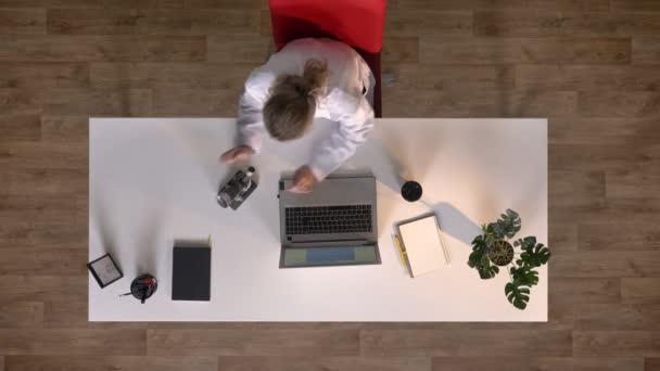 Joven científica investigando bajo microscopio y escribiendo en laptop, topshot, laboratorio médico — Vídeos de Stock