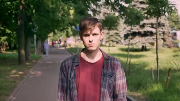 Joven hombre guapo serio está mirando en la cámara durante el día en el parque en verano, concepto urbano — Vídeo de stock