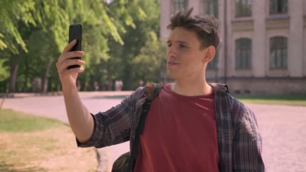 Όμορφος νεαρός έχει ένα βιντεοκλήσεων στο πάρκο στη διάρκεια της ημέρας καλοκαίρι, έννοια επικοινωνίας — Αρχείο Βίντεο