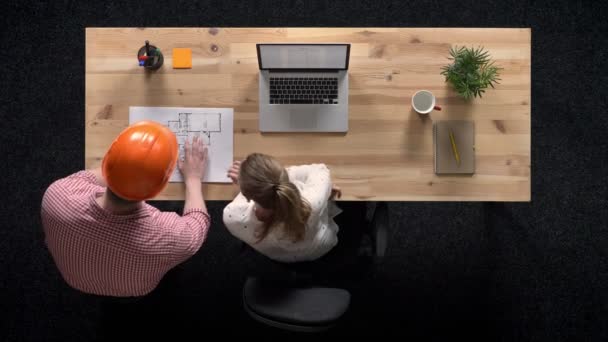 Młoda kobieta pracuje na laptopie w ciągu dnia, budowniczy przychodzi i pokazuje planu budynku, pracy koncepcja, koncepcja office, komunikacja koncepcja, top strzał — Wideo stockowe