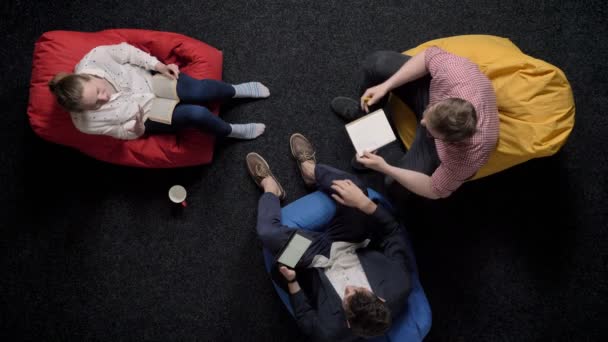 Tres trabajadores están sentados en pufs y relajante, conversación, concepto de oficina, concepto de comunicación — Vídeos de Stock