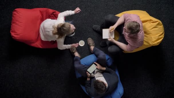 Tři pracovníci jsou sedící na poufs a relaxaci, úřad koncept, komunikační koncept, koncept týmu — Stock video