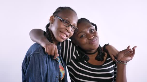 Δύο νεαρές γυναίκες αφρικανικής αμερικανικής αγκαλιάζει και να χαμογελά στη φωτογραφική μηχανή, ευτυχισμένος, απομονωμένα σε λευκό φόντο, μαύρους φίλους γέλιο — Αρχείο Βίντεο