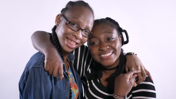 Two beautiful young african women hugging and laughing, looking at camera, happy and emotional, white studio background — Stock Video