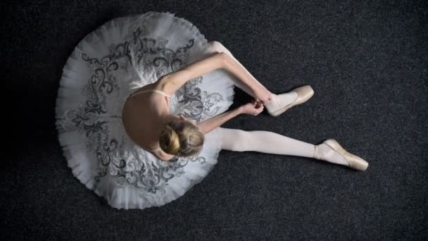 Силуэт юной балерины вяжет ленту на пуанте, сидит на полу, балетная концепция, топ-кадр — стоковое видео