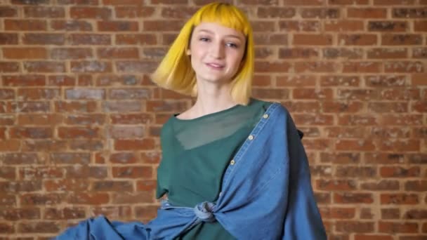 Young unusual woman with yellow hair dancing and looking at camera, isolated over brick wall background — Stock Video