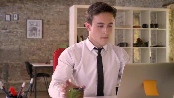 Jovem empresário feliz está trabalhando com laptop e beber café no escritório, assistindo a câmera, conceito de negócios, conceito de comunicação — Vídeo de Stock