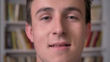 Yüz çekici işadamı gülümseyen, kamera, arka plan, kitaplık izliyor genç arka plan bulanık