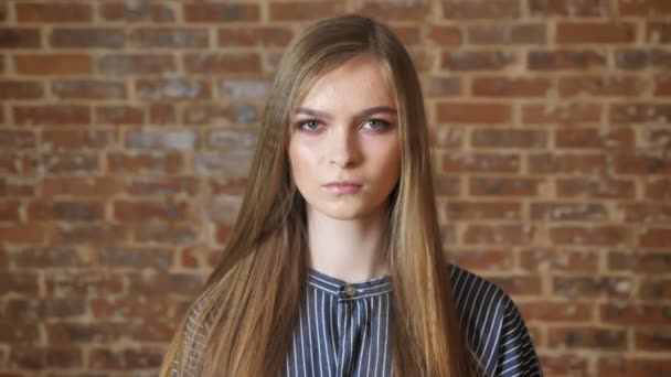 Young serious girl is watching at camera, brick background — Stock Video