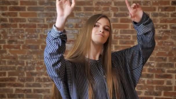 Девушка с длинными волосами танцует руками, колючая, наслаждается музыкой, кирпичным фоном — стоковое видео