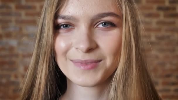 Visage de jeune femme regardant à la caméra, souriant, fond de brique, fond flou — Video