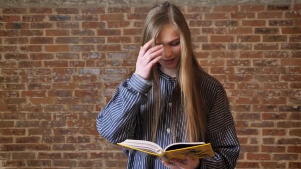 Молода красива дівчина читає книгу, розслабляючий концепт, цегляний фон — стокове відео