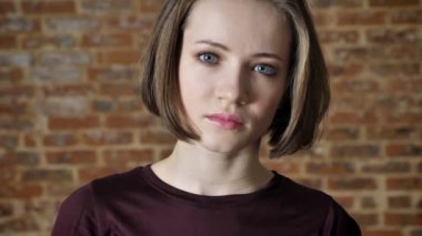 Genç güzel kendine güvenen kız kameraya, tuğla arka plan izliyor
