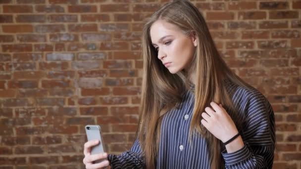 Menina bonita nova está fazendo selfie em seu smartphone, conceito de comunicação, fundo de tijolo — Vídeo de Stock