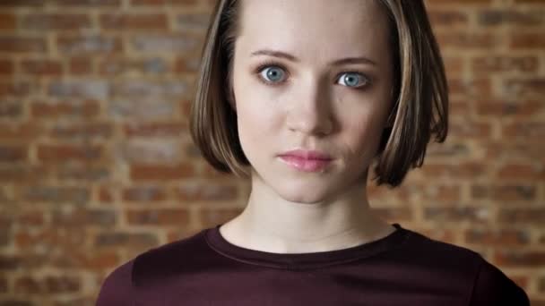 Young beautiful confident girl is watching away and then at camera, brick background — Stock Video