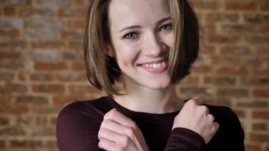 Mutlu kız gülerek, kameraya, saç, tuğla arka plan dokunmadan izlerken