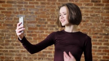 Genç güzel kız video seslenmek üstünde onun smartphone, gülümseyen, iletişim kavramı, tuğla arka plan vardır