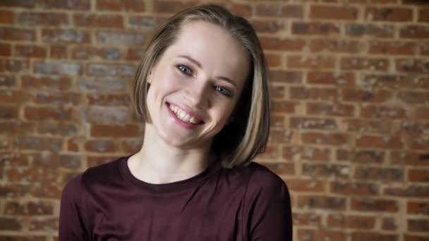 Young happy girl is giggling, watching at camera, brick background — Stock Video