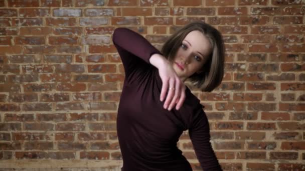 Young beautiful girl is dancing, watching at camera, movement concept, brick background — Stock Video