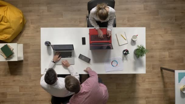 Два бизнесмена разговаривают за ноутбуком, когда женщина работает и сидит за столом в современном офисе, топшот, концепция работы — стоковое видео