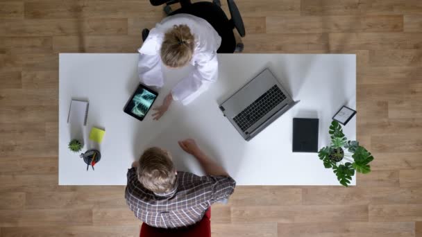 Jonge vrouw arts is x-ray scan weergeven op Tablet PC aan patiënten en ziekte, man bij de dokter, medische concept, top shot uit te leggen — Stockvideo