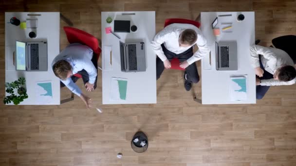 Drie jonge zakenman op werkplek toneelstuk op papier toss, rest concept, office concept, top shot — Stockvideo