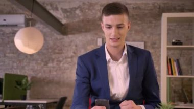 Genç çekici işadamı smartphone ofis, iyi sonuçlar nedeniyle mutlu tutarak el yumruk, Evet jest, iş kavramı, iletişim kavramı izliyor