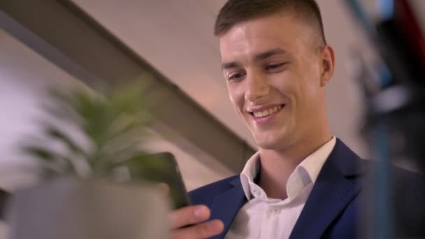 Genç çekici işadamı smartphone elinde, gülümseyen, iletişim kavramı, bulanık ön planda tutuyor — Stok video