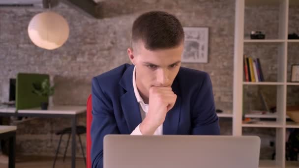 Молодой концентрированный бизнесмен смотрит ноутбук в офисе, видит хорошие результаты, держа кулак, да жест, бизнес-концепция, коммуникационная концепция — стоковое видео