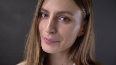 Genç çekici kız yüzünü kameraya, izlerken göz kırpıyor, kavram, gri arka plan flört