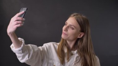 Genç güzel kız smartphone, dokunmadan saç, iletişim kavramı, gri arka plan selfie yapıyor