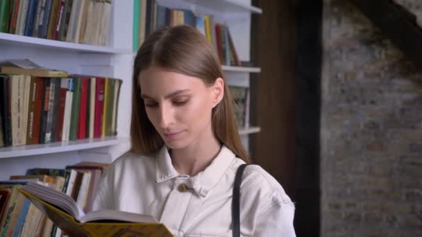 Chica Dulce Joven Está Leyendo Libro Mirando Cámara Biblioteca Fondo — Vídeo de stock