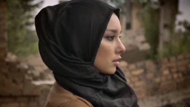 Arka planda Bina bakarak uzak ve kamera, endişeli ve korkmuş, hijab içinde genç Müslüman kadın mahvetti