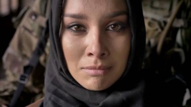 Yakın ağlıyor ve kamera, silahlı asker kadın, savaş arkasında silah duran ile bakarak hijab genç Müslüman kadın portresi