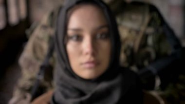 Kamera, mühimmat ve silah arkasındaki kadın, terörizm kavramı ayakta olan asker bakarak hijab üzgün genç Müslüman kadın portresi