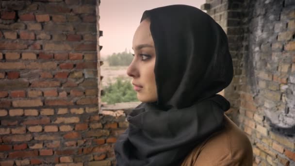 年轻哀伤的穆斯林妇女在面纱站立在被摒弃的大厦, 转动和看照相机, 恐惧和恐惧, 恐怖主义概念 — 图库视频影像