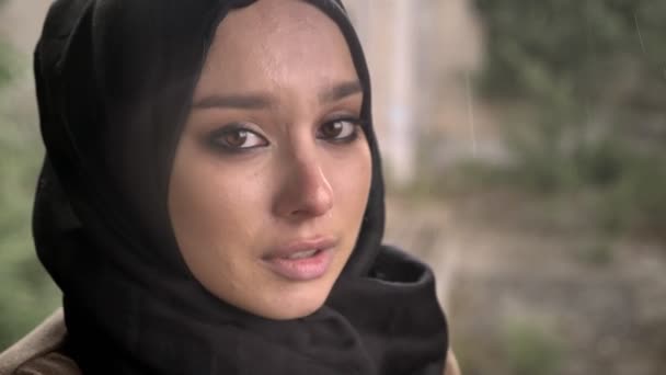 Portrait of young muslim woman in hijab looking at camera with sad depressed expression during rain — Stock Video