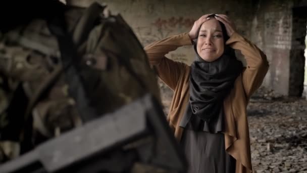 junge muslimische Frau im Hidschab schreit und weint hinter Soldat mit Munition und Waffe, steht in verlassenem Gebäude, Kriegskonzept.