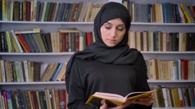 Genç ciddi Müslüman kız hijab içinde izlerken kamera, dini kavramı, kitaplık arka plan üzerinde de kitap okuma