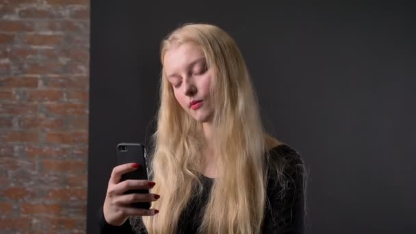 Joven linda chica rubia con lápiz labial rosa está escribiendo mensaje en el teléfono inteligente, concepto de comunicación, fondo gery — Vídeo de stock