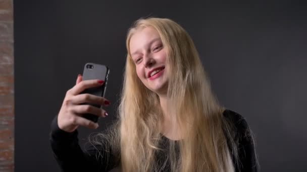 Giovane ragazza bionda carina con rossetto rosa ha una videochiamata su smartphone, concetto di comunicazione, sfondo grigio — Video Stock